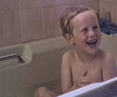A wet five-year-old Mark sitting in a bathtub and smiling.