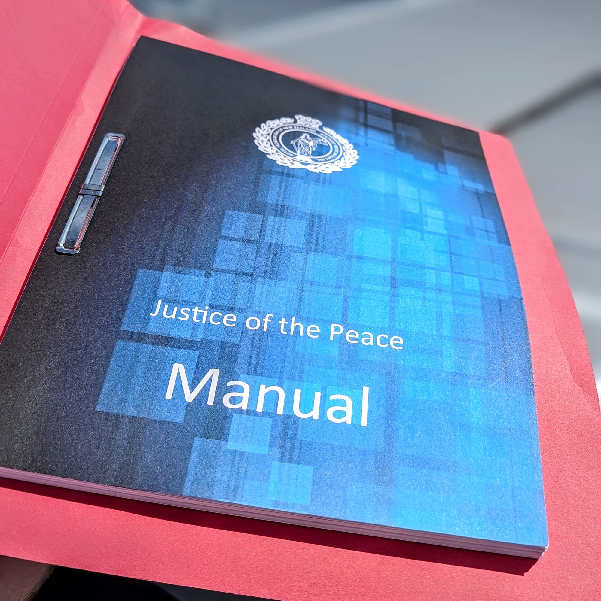 Over 100 pages neatly fastened inside a pink manila folder. The front page is blue and titled "Justice of the Peace Manual".